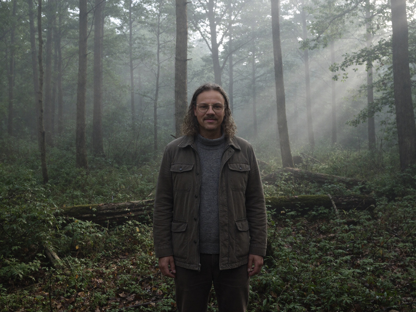 Johannes steht still zwischen hohen Bäumen im Morgennebel
